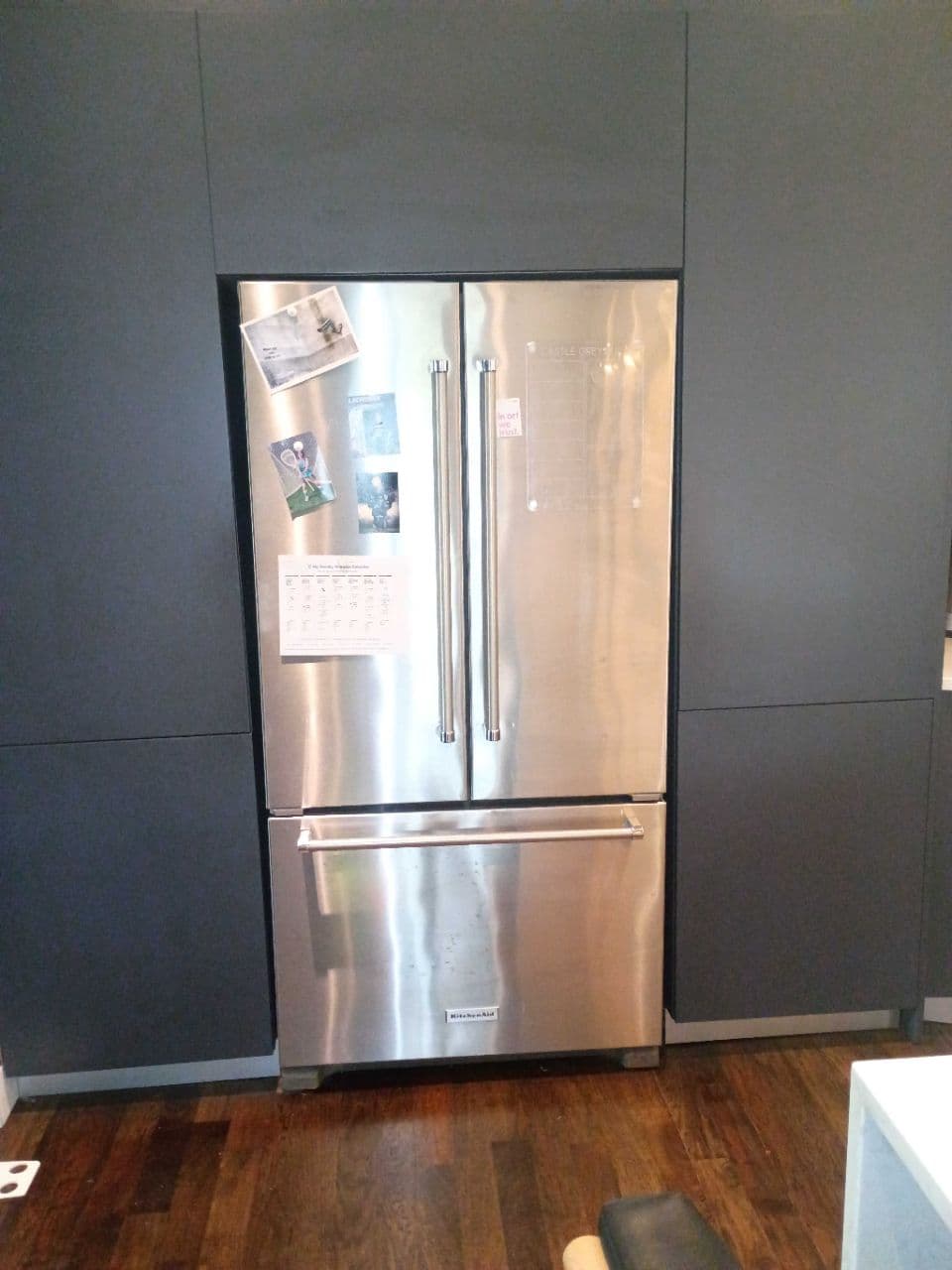 Stainless steel French door refrigerator with magnets, built into dark gray cabinetry on wood floors.